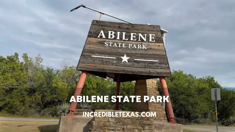 Shaded pecan grove campsites and red sandstone pavilions under morning sunlight at Abilene State Park