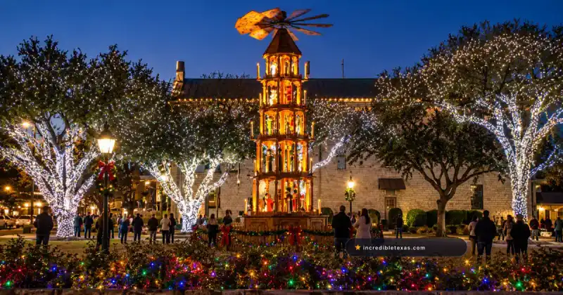 The illuminated German Christmas Pyramid at Marktplatz in Fredericksburg beneath white-lit live oaks.