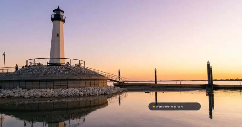 Sunset over Lake Ray Hubbard shoreline and stone lighthouse along The Harbor boardwalk in Rockwall, Texas