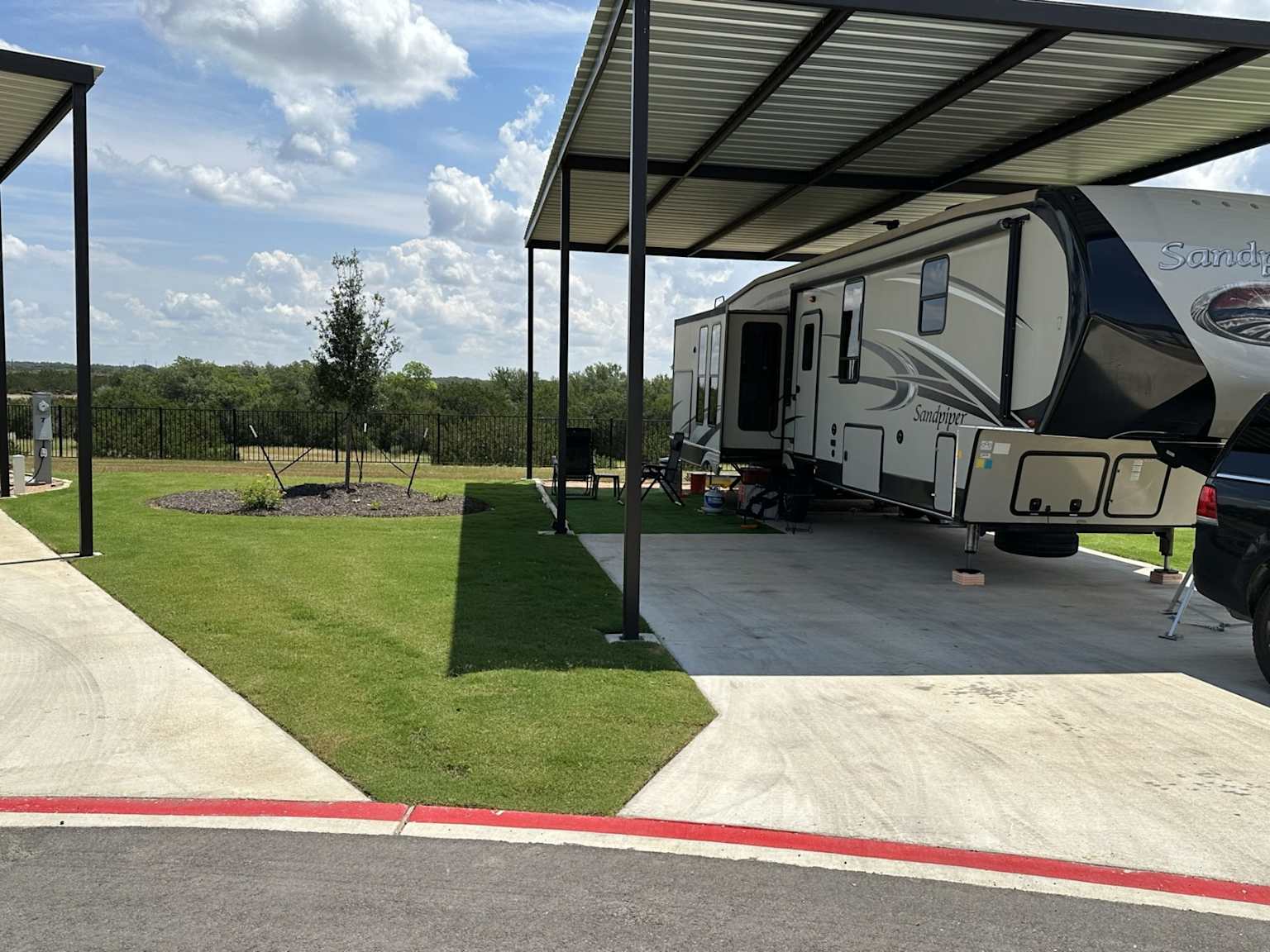 Covered RV site with concrete pad and landscaped grassy area at a modern Texas RV resort